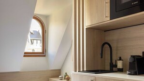 A compact bedroom with a single bed, a small bedside table, a built-in microwave, and a window with a view of a house. - Cozy Studio A/C 1P - Arc de Triomphe (Paris)