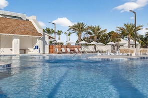 A swimming pool with lounge chairs and umbrellas, surrounded by palm trees and a modern building. - Landing | Modern 3BD, Gym (Santa Rosa Beach)