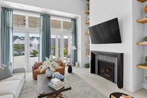 A modern living room with a fireplace, a flat-screen TV, and a view of a lake. - Landing | Modern 3BD, Gym (Santa Rosa Beach)