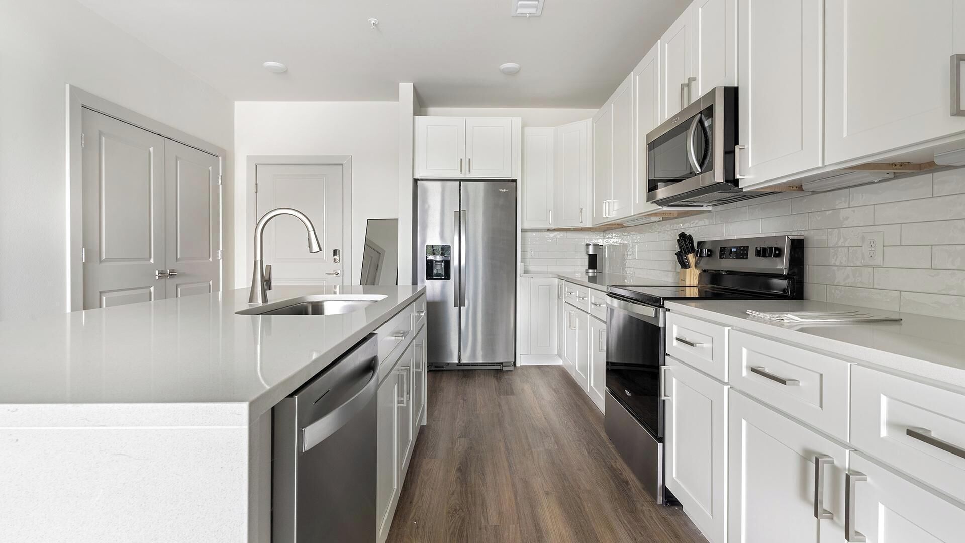 A modern kitchen with white cabinetry, stainless steel appliances, and a wooden floor.