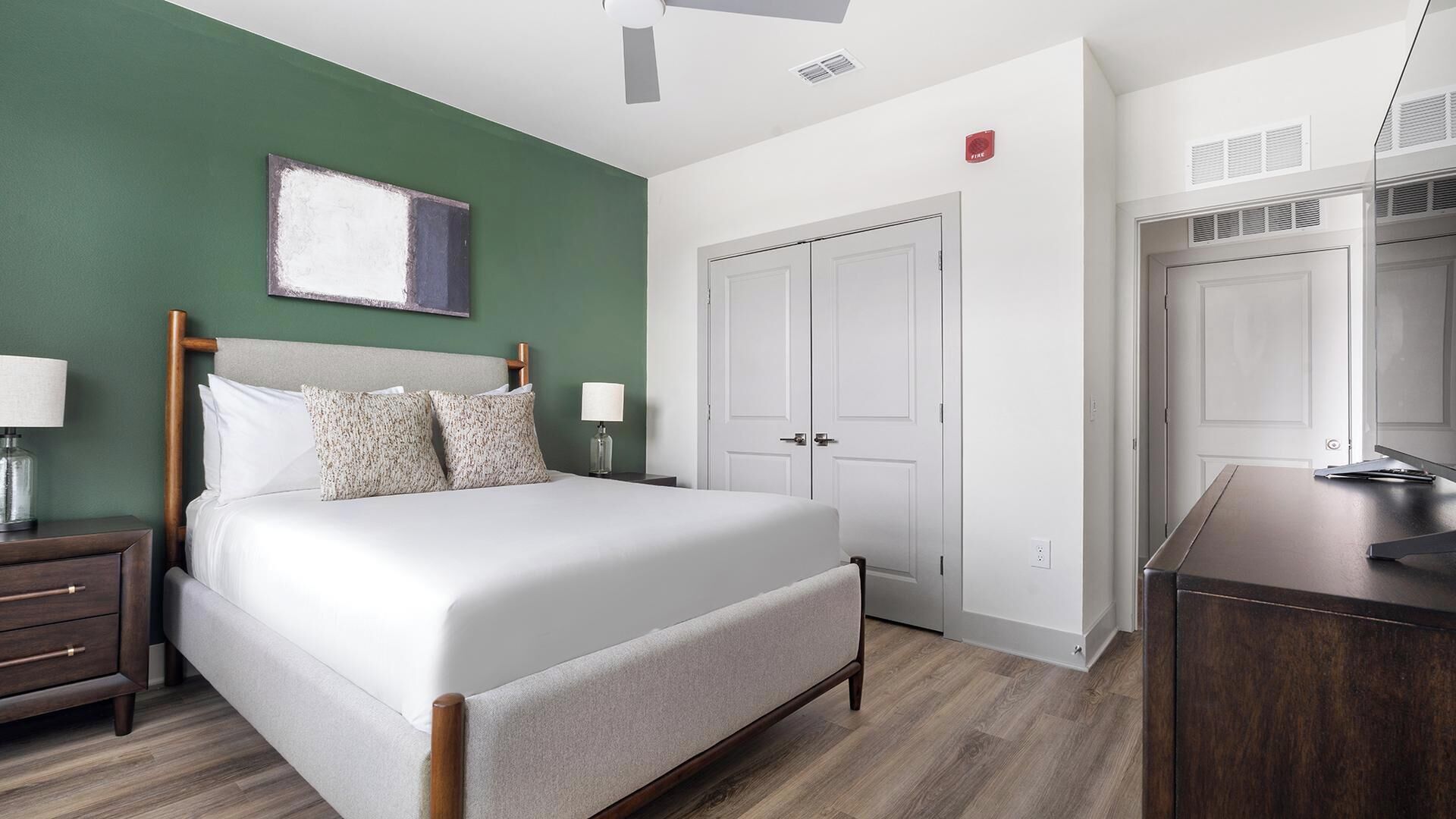 Quarto de hotel com cama, mesa de cabeceira, abajur e um quadro na parede.
