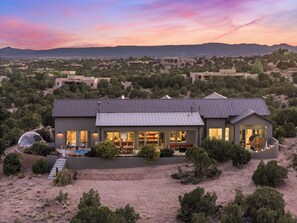 Una casa moderna con un amplio frente de cristal, una zona de estar cubierta al aire libre y vistas del paisaje circundante.