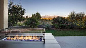 A modern outdoor fire feature with a clear view of a landscaped garden and distant mountains. - Santa Fe Design Home · Stargazing Dome, Sauna, Cold Plunge & Mountain Views (Santa Fe)
