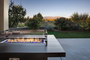Una moderna estructura para fuego al aire libre, con vista despejada a un jardín ajardinado y montañas distantes.