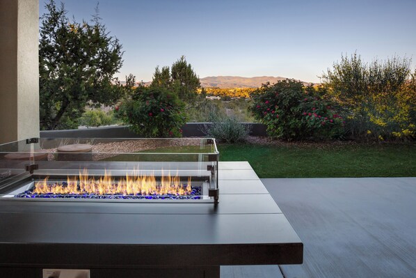 Una moderna estructura para fuego al aire libre, con vista despejada a un jardín ajardinado y montañas distantes.