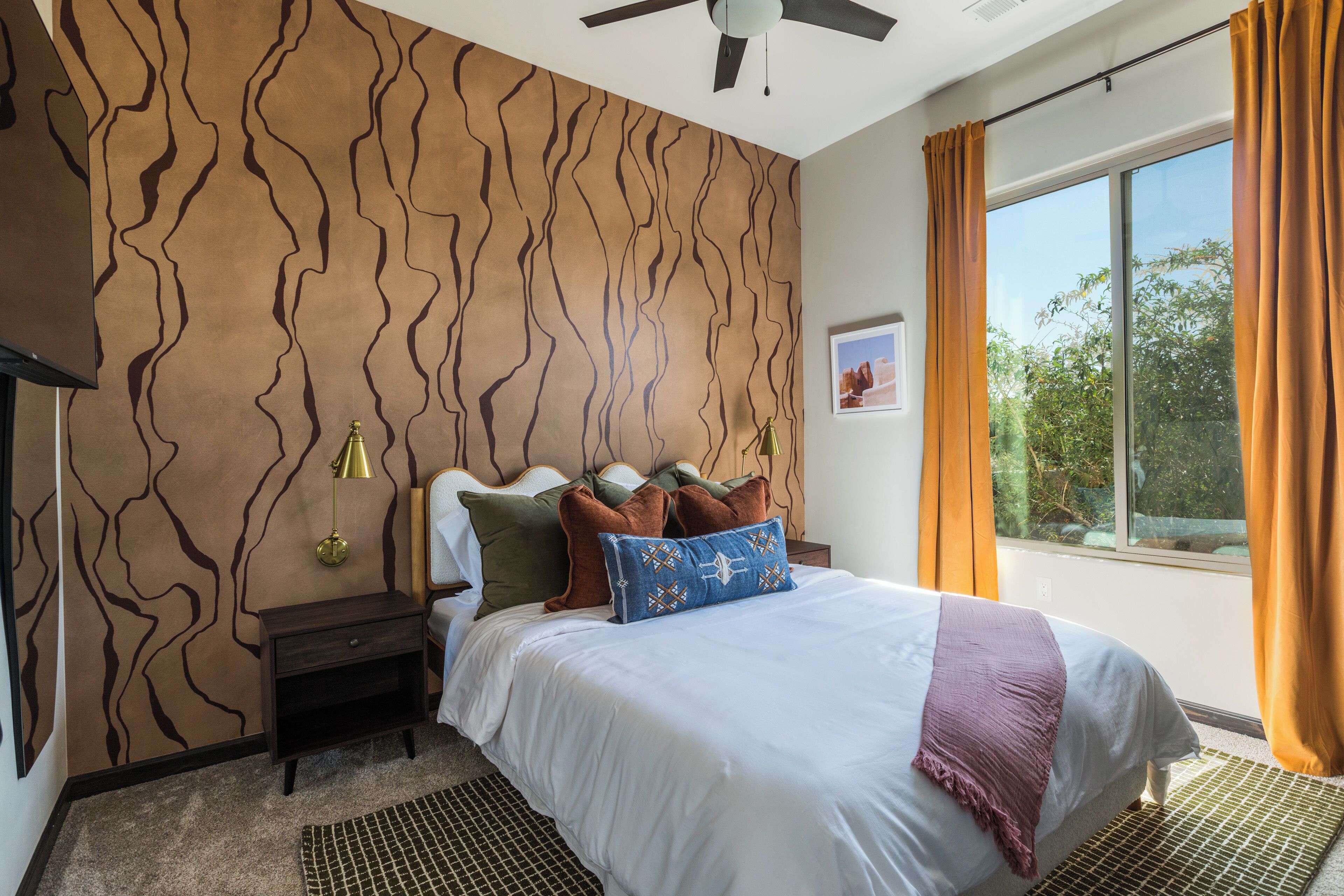 A bedroom with a bed, nightstands, a ceiling fan, a window with curtains, and a wall with a wavy pattern.