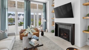 A modern living room with a fireplace, a flat-screen TV, and a view of a lake. - Landing | Stylish 2BD, Gym (Santa Rosa Beach)
