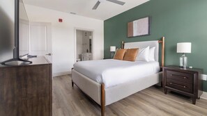 A hotel room with a bed, bedside table, lamp, and a desk with a chair. - Landing | Stunning 2BD, Gym (Santa Rosa Beach)