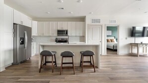 A modern kitchen with white cabinets, a stainless steel refrigerator, a microwave, and a bar area with stools. - Landing | Stylish 2BD, Gym (Santa Rosa Beach)