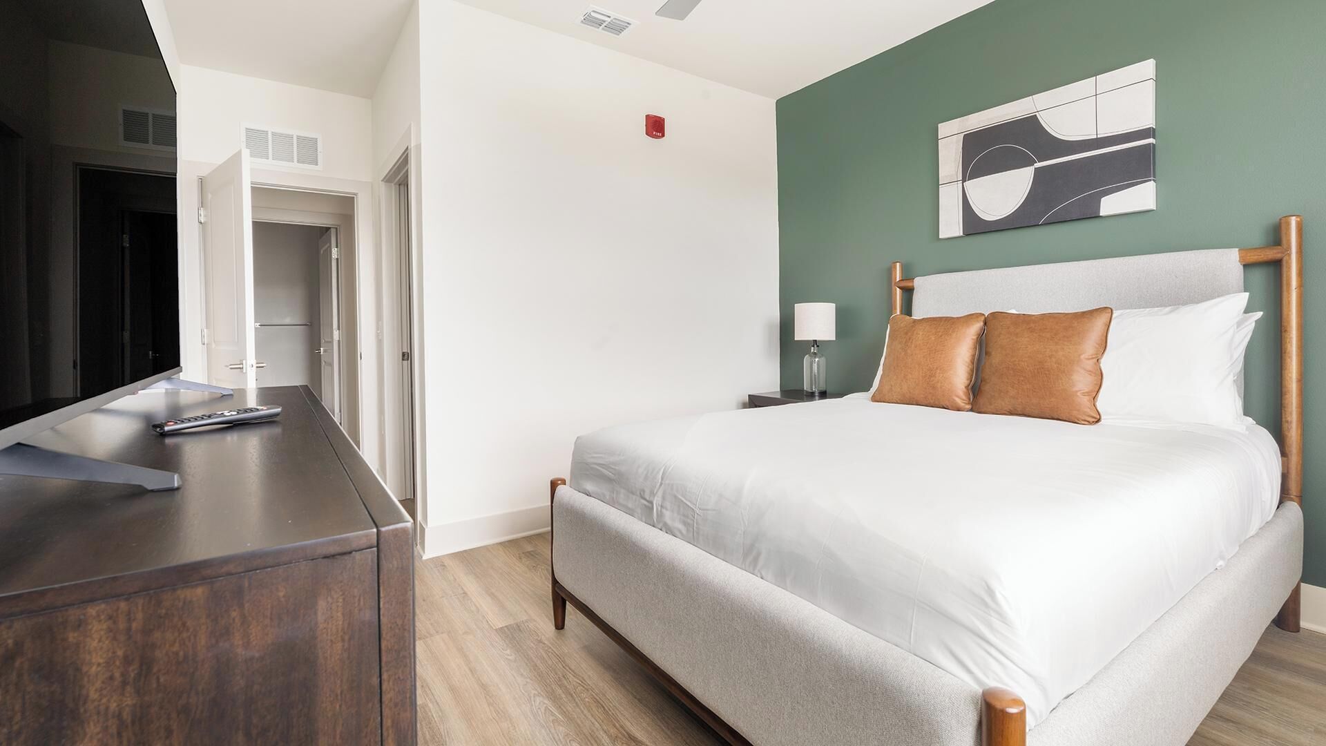 A hotel room with a bed, bedside table, lamp, and artwork on the wall.