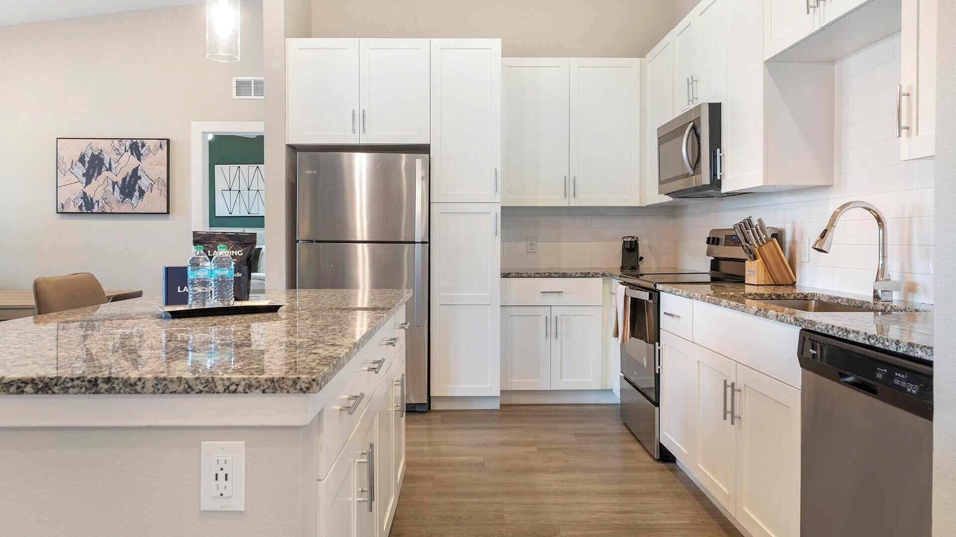 A modern kitchen with white cabinets, stainless steel appliances, granite countertops, and a central island.