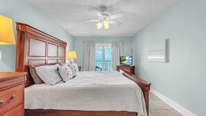 A bedroom with a wooden bed, a ceiling fan, a TV, and a view of the outdoors. - Direct Beachfront Condo with Amazing Gulf Views! Pool, Grill, Free Wi-Fi & Parking! ~ 204 Seagate (Indian Rocks Beach)