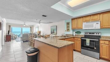 A spacious kitchen with granite countertops, wooden cabinets, a large island, and a stainless steel oven.