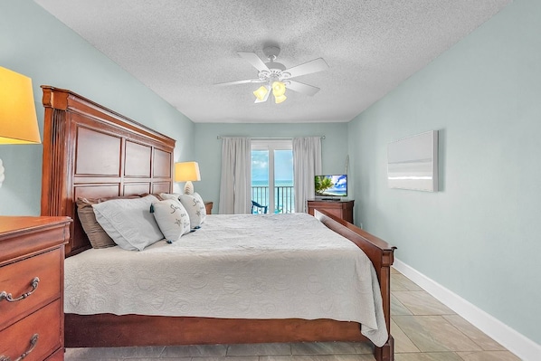 A bedroom with a wooden bed, a ceiling fan, a TV, and a window with curtains.