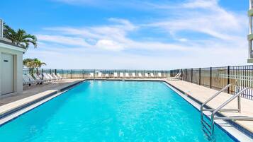 A swimming pool with lounge chairs and a metal railing, surrounded by a fence.