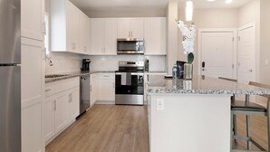 A modern kitchen with white cabinets, stainless steel appliances, a granite countertop, and a wooden floor. - Landing | Modern 1BD, Clubhouse, Pool (Orlando)