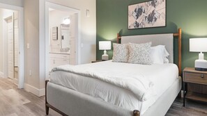 A neatly arranged bedroom with a bed, bedside tables, a nightstand, a lamp, and a painting on the wall. - Landing | Modern 2BD, Clubhouse, Pool (Orlando)