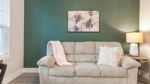 A room with a green wall, a striped sofa, a white lamp, and a framed abstract artwork. - Landing | Incredible 1BD, Gym, Clubhouse (Orlando)