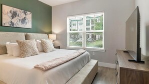 A bedroom with a bed, pillows, a bedside table, a lamp, a window, and a TV. - Landing | Incredible 1BD, Gym, Clubhouse (Orlando)