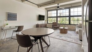 Un ambiente ufficio moderno con un tavolo rotondo, sedie, una scrivania, una televisione e ampie finestre.