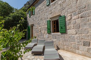 A stone building with a courtyard, green shutters, and lounge chairs. - Amazing Villas in Omis for 8 (Omis)