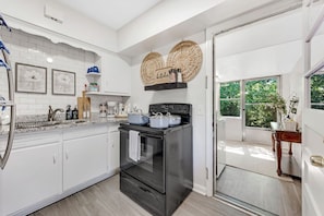 A kitchen with white cabinets, a black stove, and a window with a view of greenery. - Midtown Luxury | 10 min to Ft. Benning (Columbus)