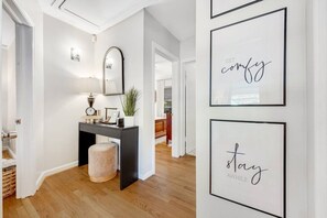 A hallway with a black console table, a round ottoman, a mirror, and framed inspirational quotes on the wall. - Midtown Luxury | 10 min to Ft. Benning (Columbus)