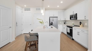 A modern kitchen with white cabinetry, a central island, a stainless steel refrigerator, and a built-in oven. - Landing | Stunning 1BD, Clubhouse, Courtyard (Dallas)