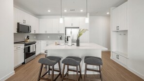 A modern kitchen with white cabinets, a central island with bar stools, a microwave, and a coffee machine. - Landing | Amazing 2BD, Pool, Gym (Dallas)