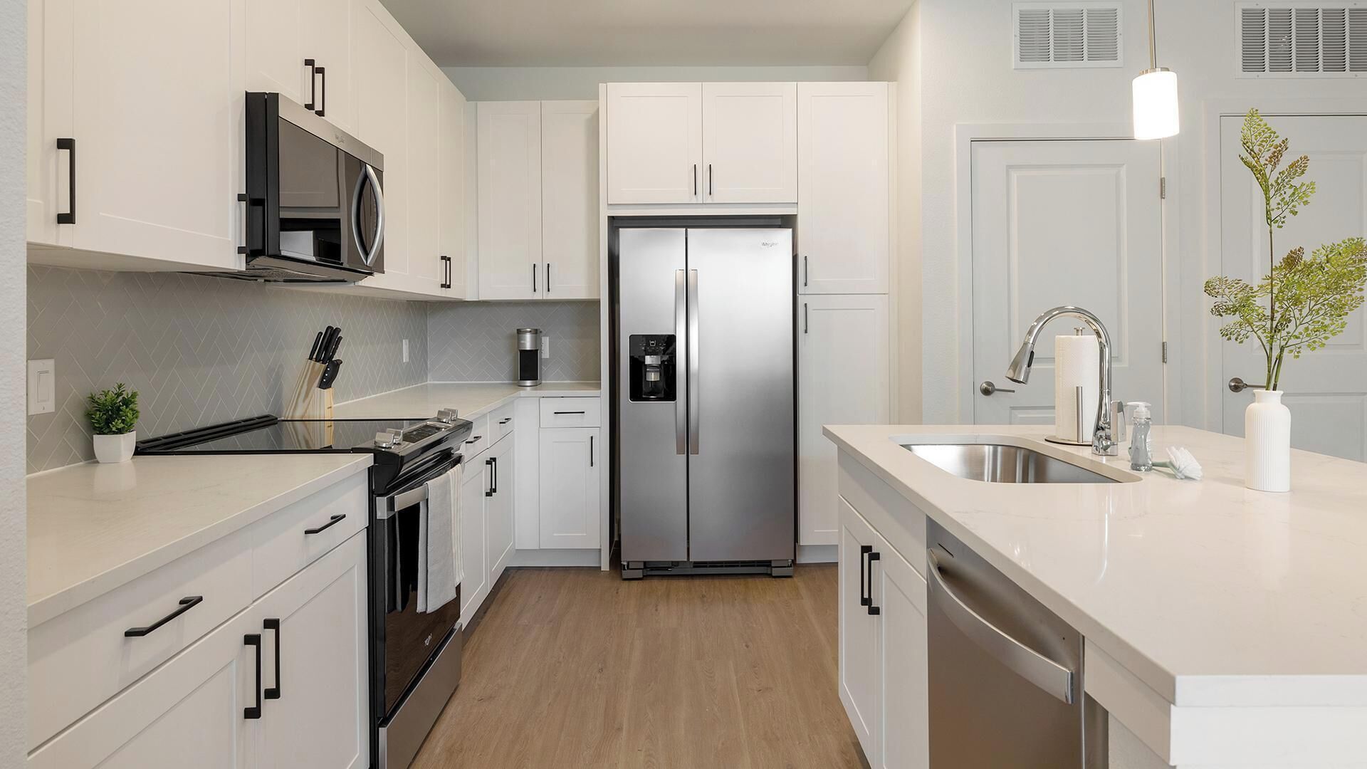 Une cuisine moderne avec des meubles blancs, des appareils en acier inoxydable et un plancher en bois.