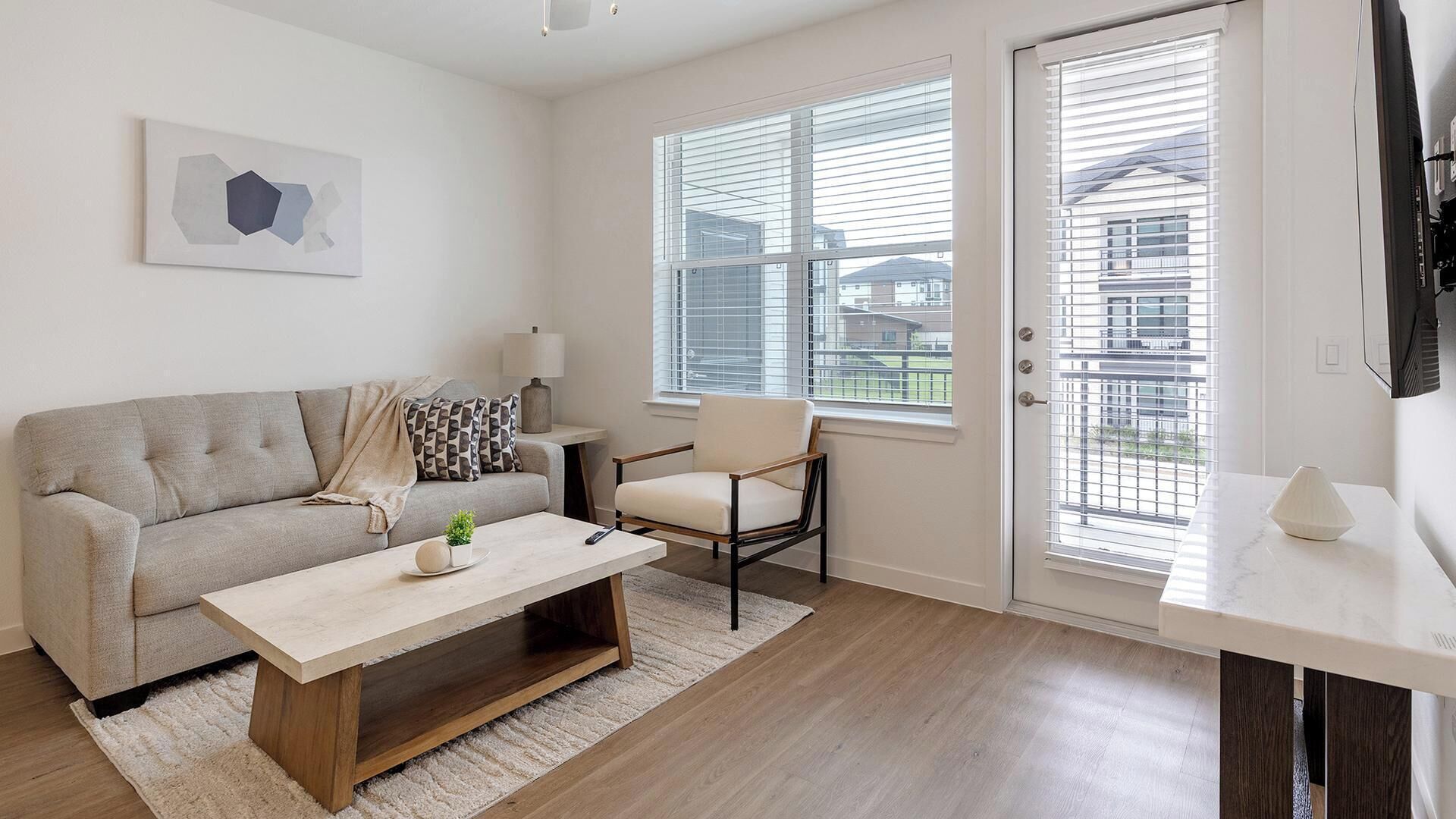 Un salon moderne comprenant un canapé, une table basse, un fauteuil et une grande fenêtre équipée de stores.