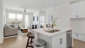 Uma cozinha moderna com uma ilha central, uma área de refeições com sofá e mesa, e uma sala de estar com sofá e televisão.