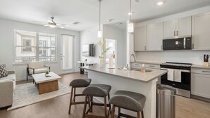 A modern kitchen with a central island, stainless steel appliances, and a dining area with a sofa and chairs. - Landing | Amazing 1BD, Gym, Clubhouse (Dallas)
