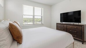Ein Schlafzimmer mit einem Bett, einem Schminktisch, einem Fernseher und einem Fenster mit Jalousien.
