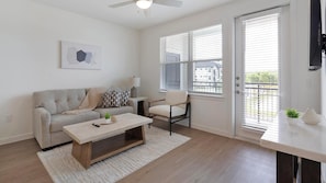 A living room with a sofa, a chair, a coffee table, and a TV. - Landing | Beautiful 1BD, Gym, Pool (Dallas)