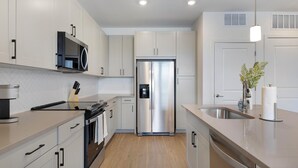 A modern kitchen with stainless steel appliances, white cabinetry, and a wooden floor. - Landing | Beautiful 1BD, Courtyard, Clubhouse (Dallas)