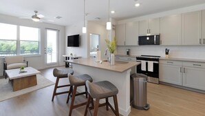 A modern kitchen with a central island, bar stools, a TV, and a microwave. - Landing | Chic 1BD, Clubhouse, Gym (Dallas)