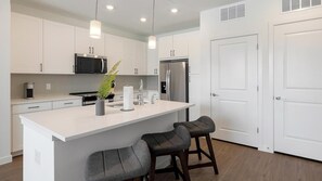 A modern kitchen with white cabinetry, stainless steel appliances, and a central island with bar stools. - Landing | Incredible 1BD, Pool, Gym (Dallas)