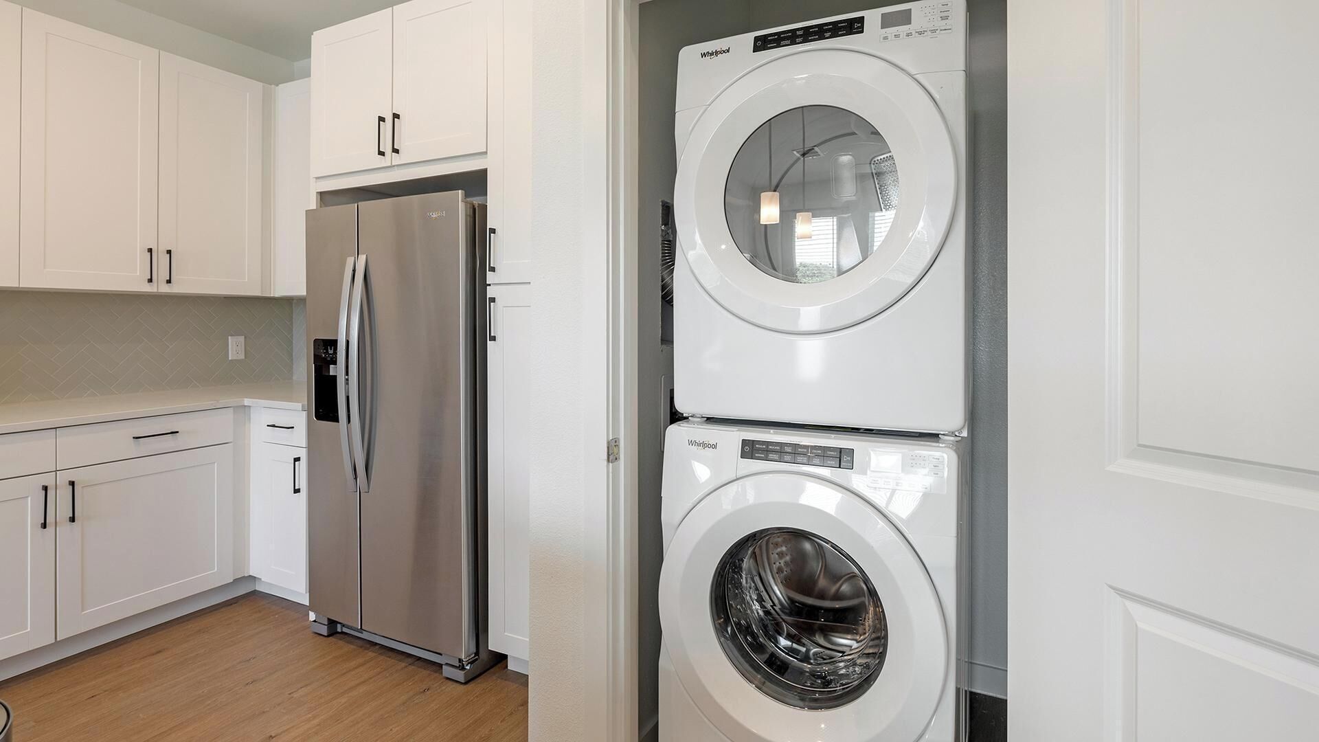 A kitchen with white cabinets, a stainless steel refrigerator, and a stacked washer and dryer.