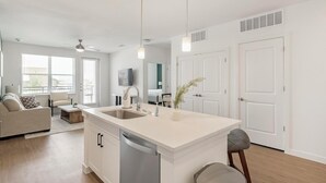 A modern kitchen with a central island, a dining area with a sofa and table, and a living room with a TV. - Landing | Stylish 2BD, Courtyard, Clubhouse (Dallas)