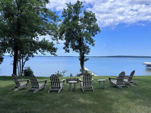 Un área de descanso junto al lago con sillas Adirondack y una pequeña mesa, rodeada de árboles y vistas al agua.