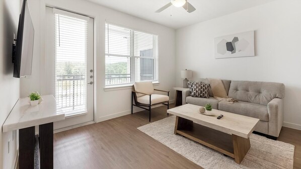 Ein modernes Wohnzimmer mit Sofa, Couchtisch, Sessel, Fernseher und einem Gemälde an der Wand.