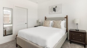 Ein Schlafzimmer mit Bett, Nachttischen, einer Lampe, einem Spiegel, einer Tür und einem Wandbild.
