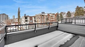 A balcony with a view of residential buildings, a metal railing, and snow on the ground. - 105-Urban Retreat / Stylish-brand-new modern home (Calgary)