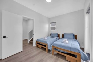 A bedroom with two beds, a wooden floor, a white door, and a window with blinds. - 105-Urban Retreat / Stylish-brand-new modern home (Calgary)
