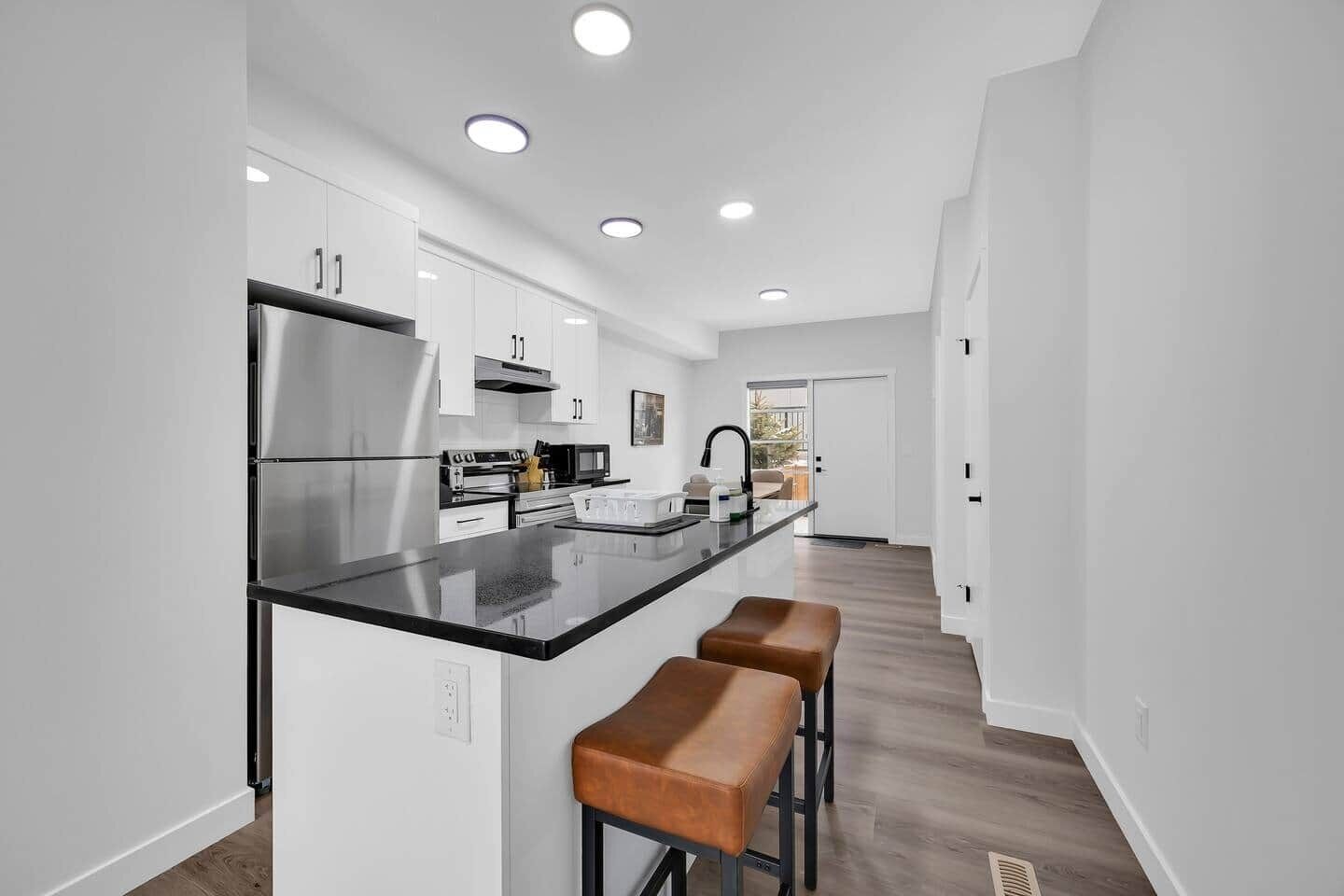A modern kitchen with a central island, white cabinetry, and a wooden floor.