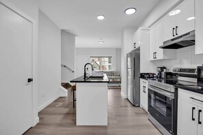 A modern kitchen with white cabinetry, a central island, and built-in appliances. - 105-Urban Retreat / Stylish-brand-new modern home (Calgary)