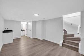 Ein geräumiger Raum mit Holzboden, weißen Wänden, einer Küchenzeile und einer Treppe.