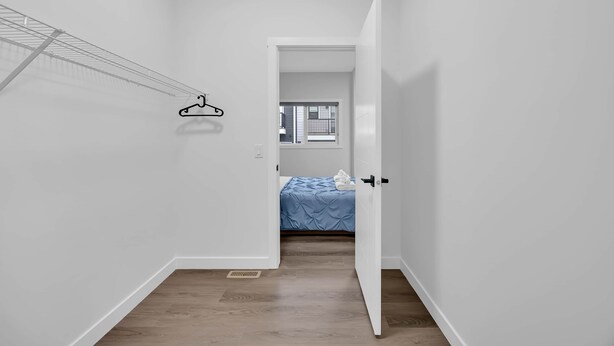 A narrow hallway with a clothes rack, a door leading to a bedroom with a bed, and a window. - Crescent Heights Hideout. (Calgary)