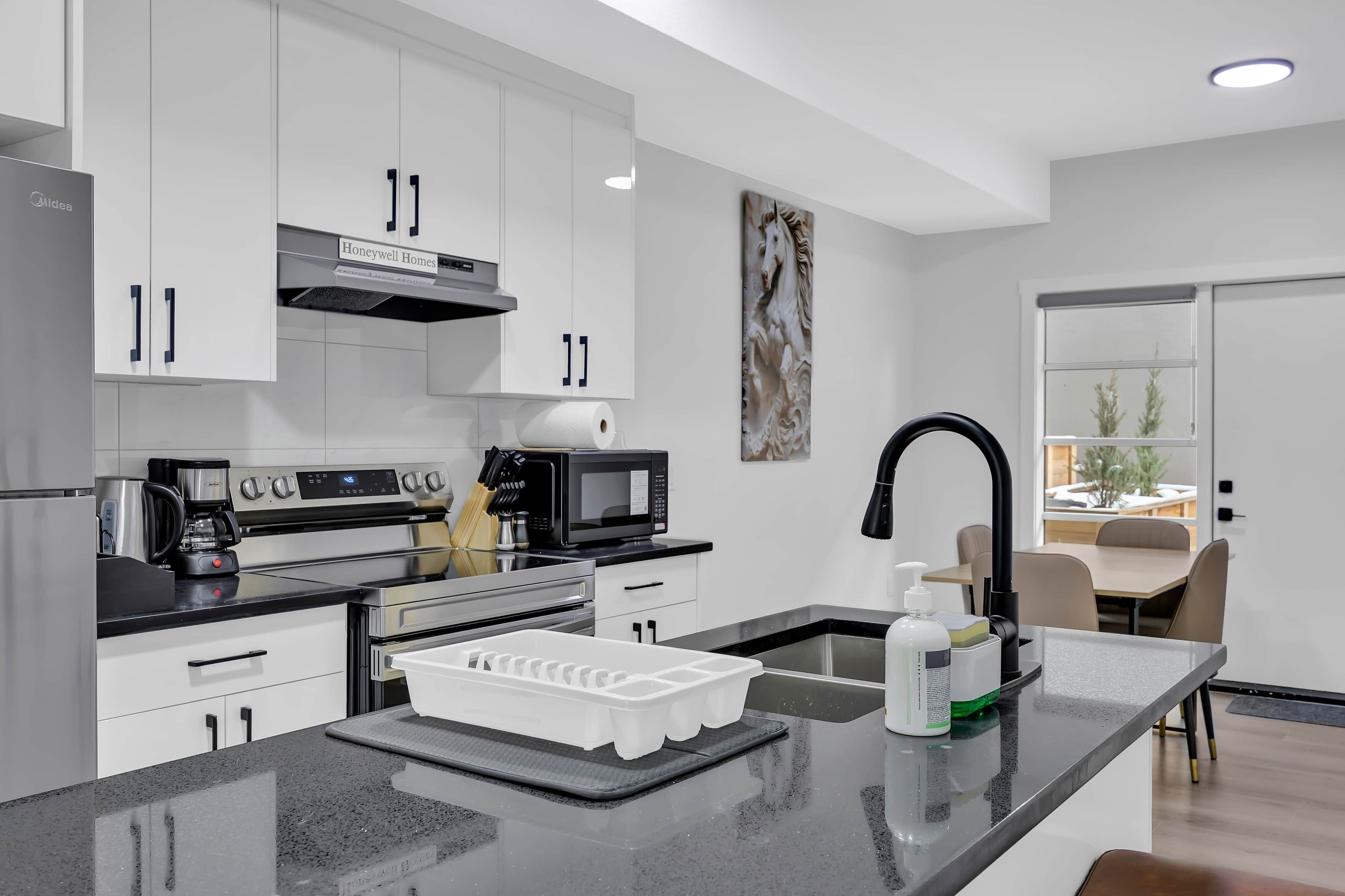 A modern kitchen with white cabinets, stainless steel appliances, a black countertop, and a view to the dining area.